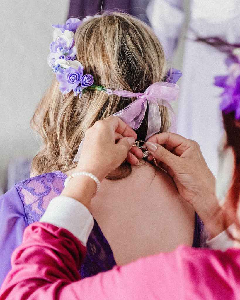 A bridesmaid being fitted with a lavender floral crown before a wedding ceremony.