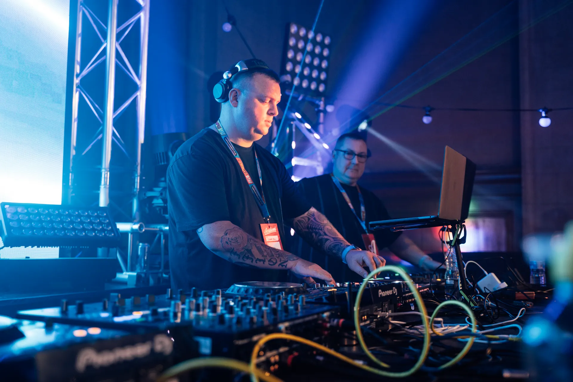 DJ at the Pioneer decks under blue stage lights — Academi Summer Ball 2024 main hall.