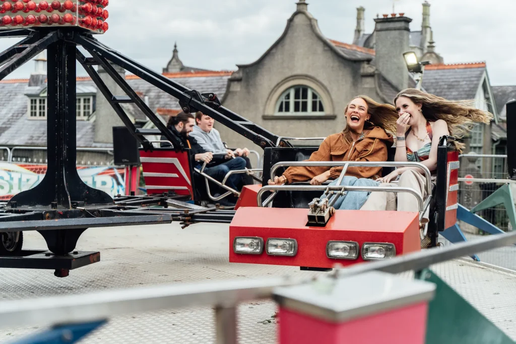 Bangor University students laughing on a fairground ride during the daytime takeover — Academi Summer Ball 2024.