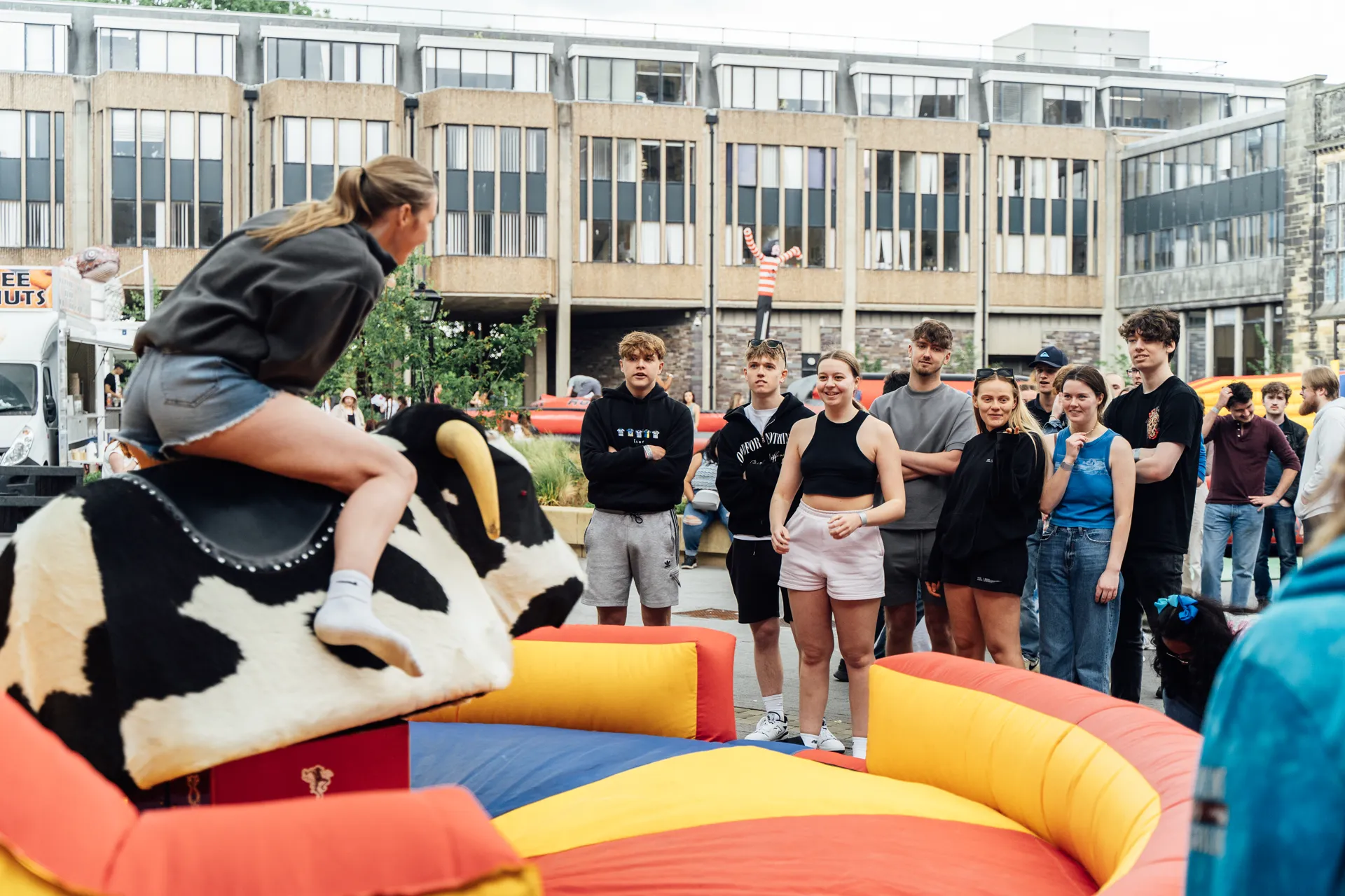 Mechanical bull crowd-watching in the Pontio courtyard — daytime activity at the Academi Summer Ball 2024.