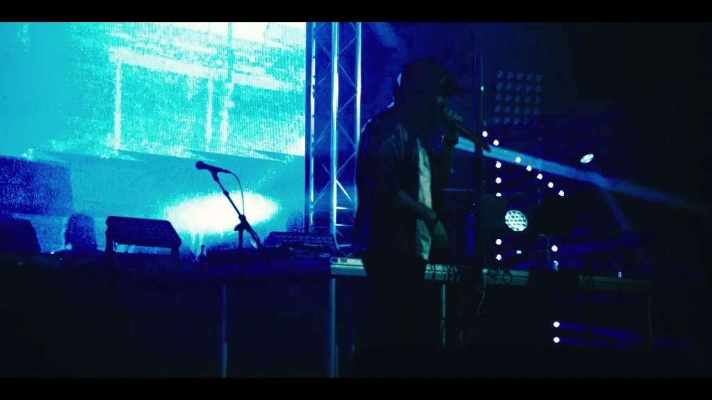 Eminem tribute artist silhouetted on stage in blue par-can wash with bright LED screen behind — live show promo for booking.