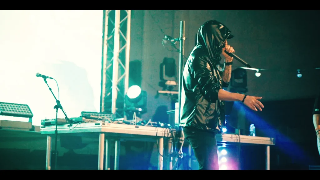 Hooded artist holds a microphone front-of-stage in front of a high-resolution LED wall — Eminem tribute live-show promo film.