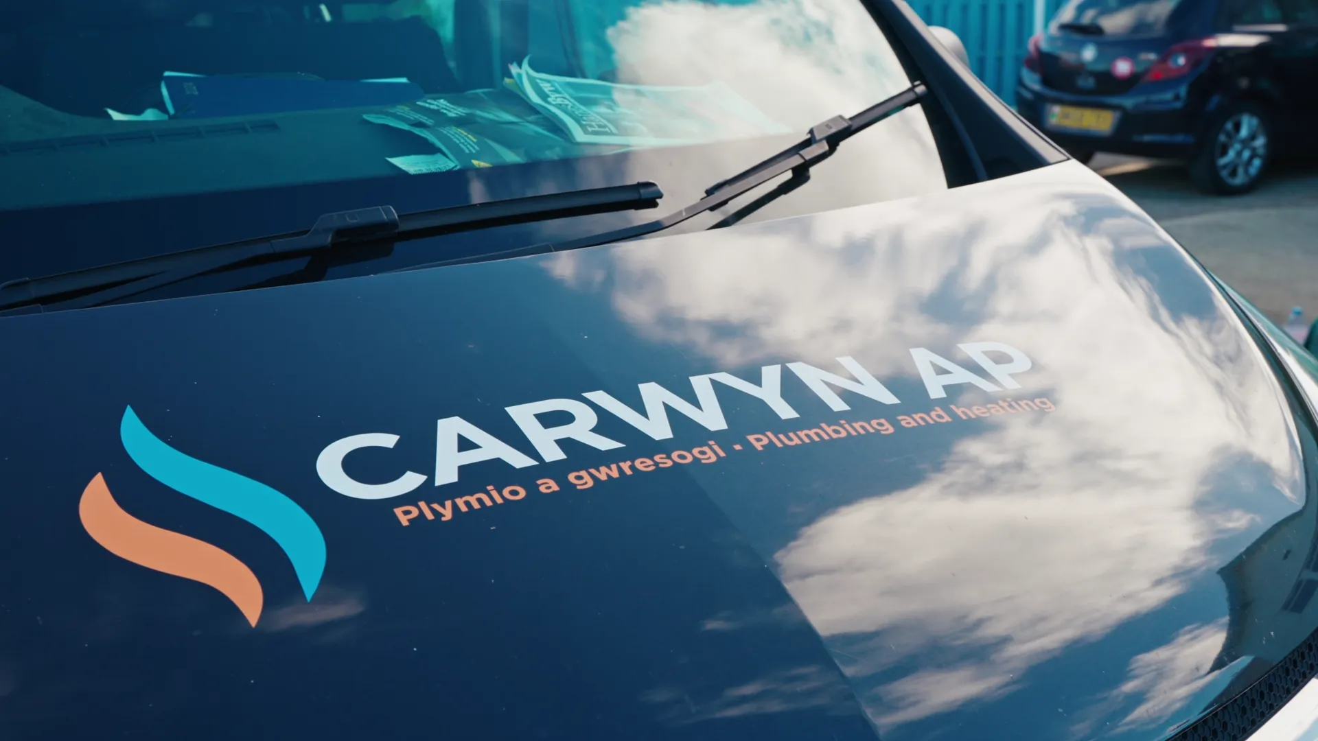Carwyn AP plumbing-and-heating logo on a van bonnet with sky reflected in the paint — branding detail for the Menter Môn case study.