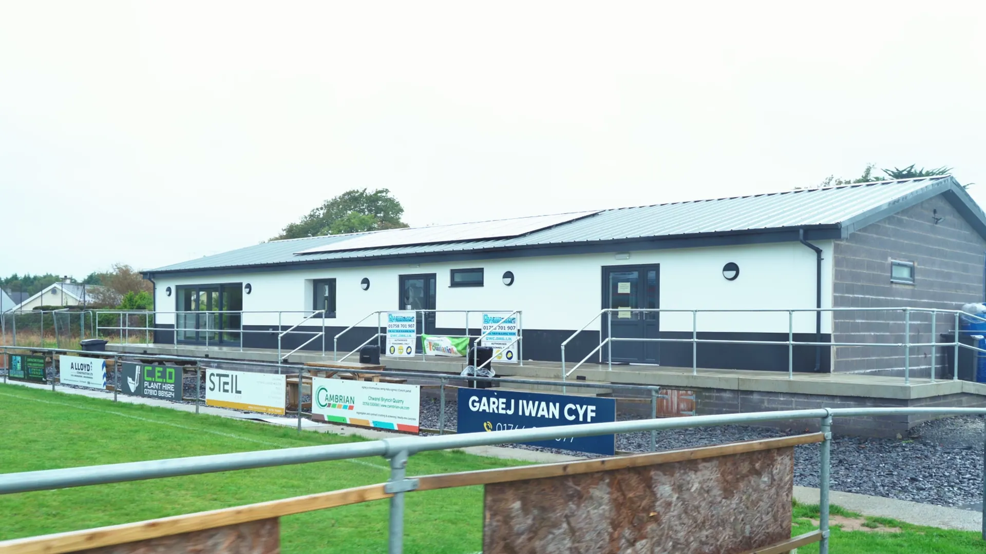 New CPD Pwllheli clubhouse with local sponsor boards — CED Plant Hire, Cambrian, Garej Iwan Cyf — Llŷn Peninsula grassroots football.