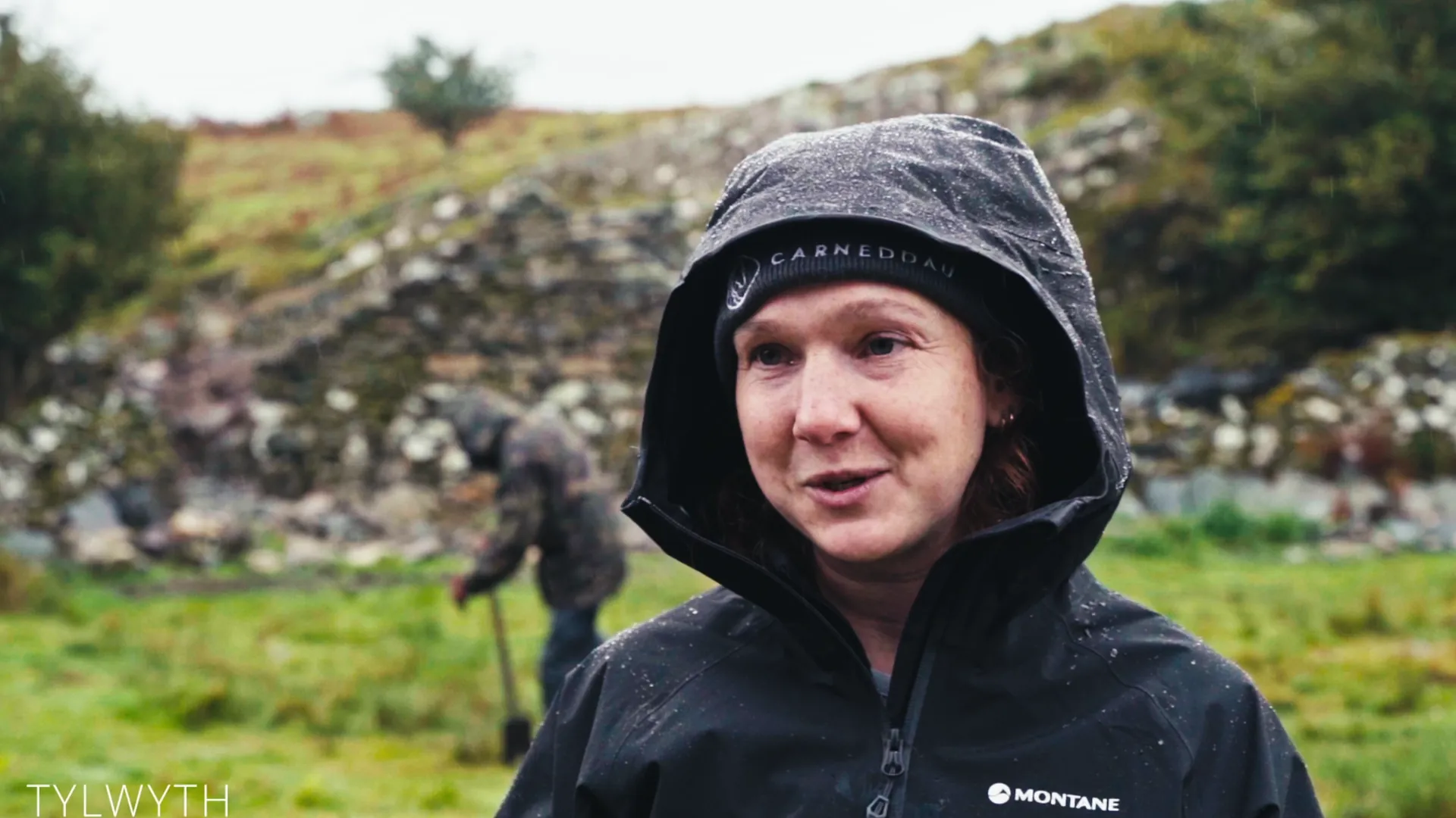 Tylwyth project lead interviewed in horizontal rain in a CARNEDDAU waterproof hood — community archaeology film for Menter Môn, Harlech uplands.