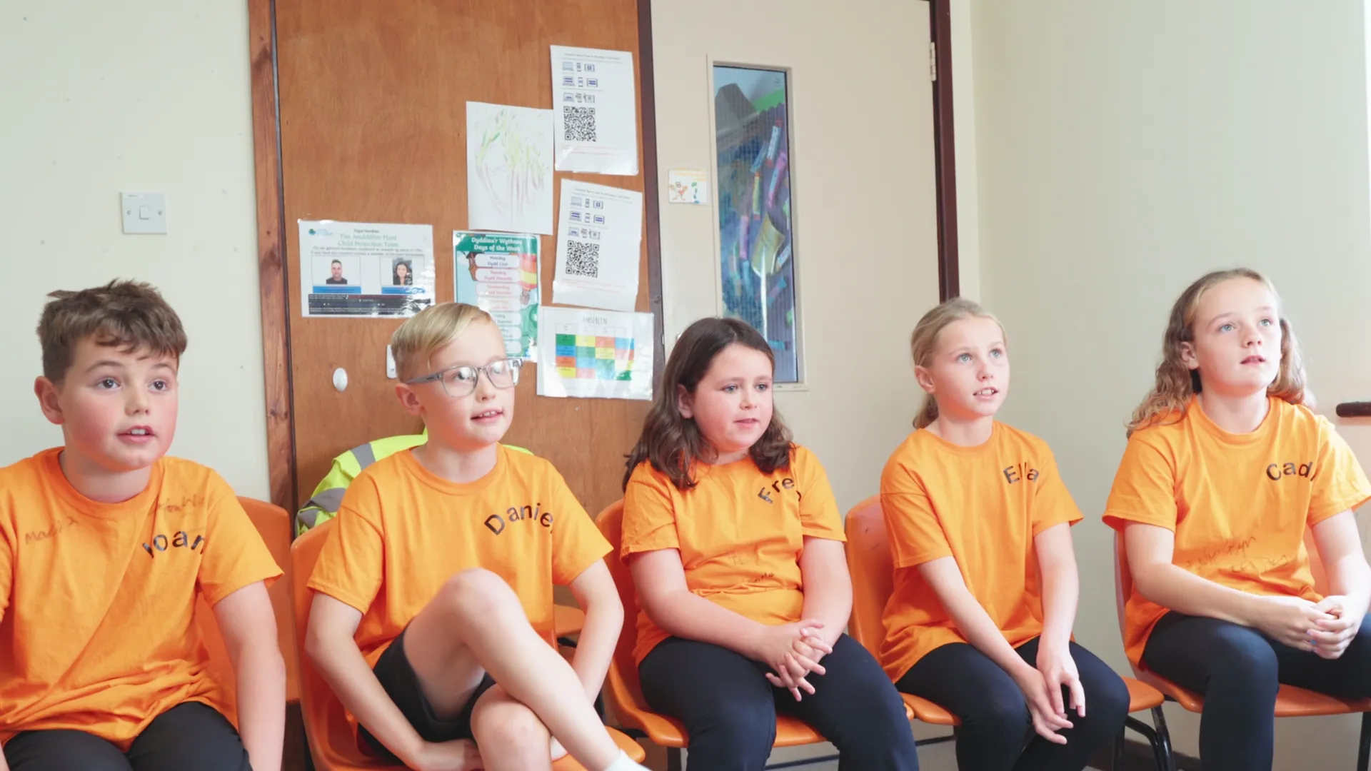 Five Ysgol Henblas pupils interviewed in matching orange Hwyl Henblas t-shirts about organising their own music festival — Mona Digital for Menter Môn.