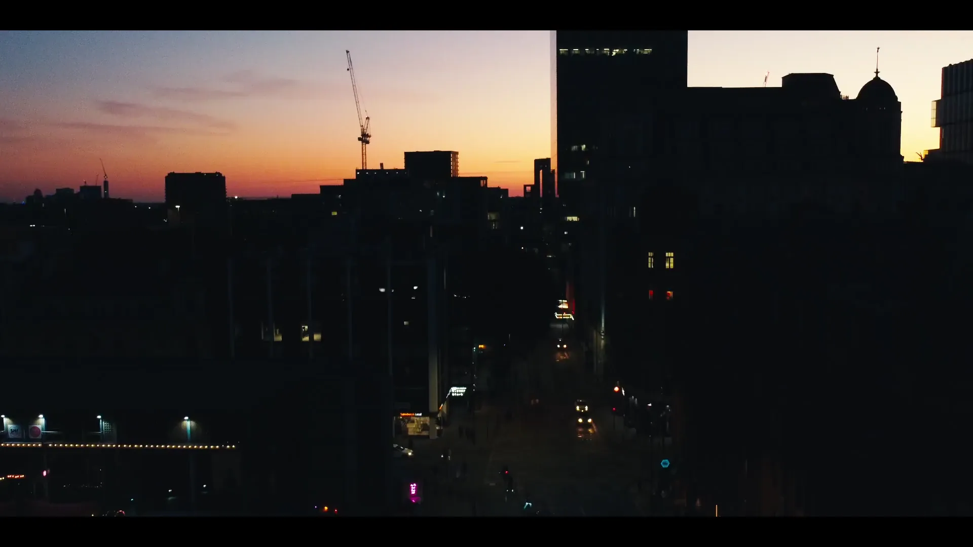 Welsh urban cityscape at sunset with construction cranes silhouetted against an orange sky — drone showreel opening frame, Mona Digital.