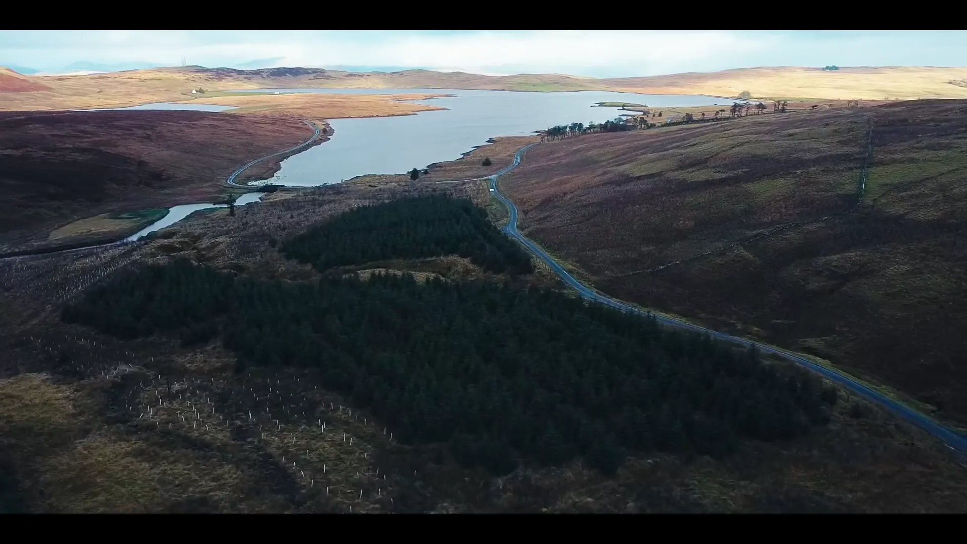 Welsh upland reservoir cradled between heather moorland and a pine-forest plantation — drone showreel landscape from Mona Digital.